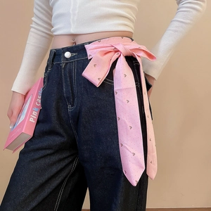 Close-up of pink silk ribbon belt tied as a bow on dark blue jeans for a stylish look