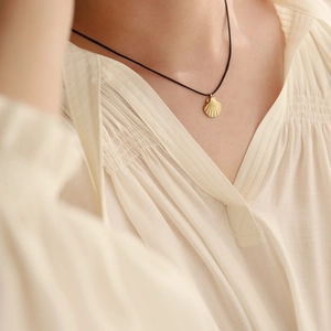Golden shell pendant necklace with black cord on model, coastal vacation style jewelry