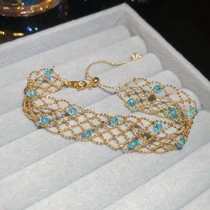 Detail view of a gold crystal beaded mesh bracelet with light blue gemstones on a jewelry tray