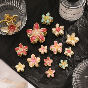 Flat lay of colorful enamel plumeria hair claws in various sizes on black fabric