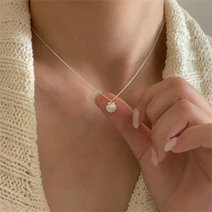 Close-up of minimalist shell pendant necklace in 925 silver worn on a beige sweater