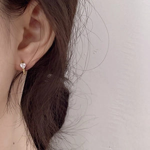 Close-up of a gold heart-shaped zircon earring worn to show its size and elegant style