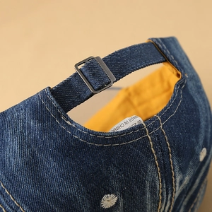 Detailed close-up showing adjustable metal buckle and white embroidery on blue denim cap