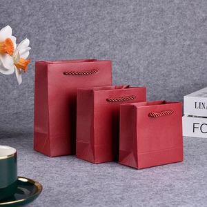 Three sizes of red textured paper gift bags with twisted handles on a grey surface