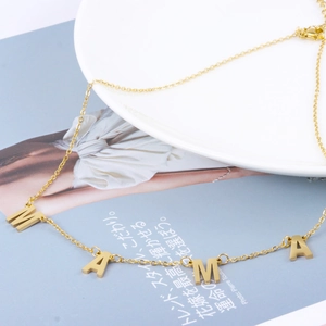 Detailansicht der goldenen MAMA Buchstaben-Anhänger an einer feinen Kette auf Lifestyle-Hintergrund