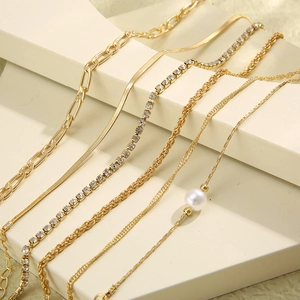 Detail of five layered gold bracelets with figaro, snake, and tennis chain textures
