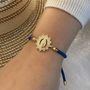 Detail of blue braided rope bracelet with gold Virgin Mary charm and white zircon inlay
