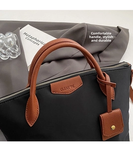 Detail of black nylon tote with premium brown leather handles and brand logo patch