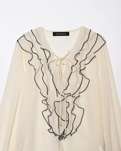 Dettaglio della camicetta in chiffon a balze con bordo nero e laccetti sullo scollo a V