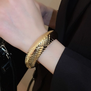 Détail d'un large bracelet doré avec textures en V sur le poignet d'un mannequin chic