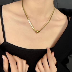 Detailed view of layered gold snake chain and bead necklace with central gold ball pendant