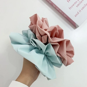 Detailed view of large pink and light blue pleated satin hair scrunchies held in hand