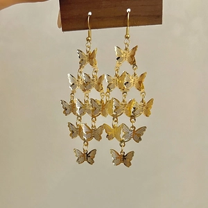 Détail de boucles d'oreilles pampilles papillon dorées sur présentoir en bois foncé