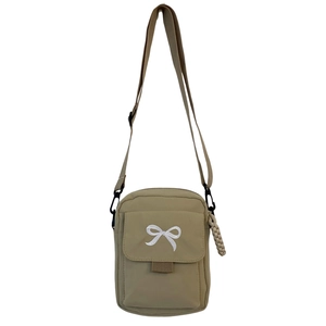 Detailed view of the khaki crossbody bag featuring a white embroidered bow and zipper