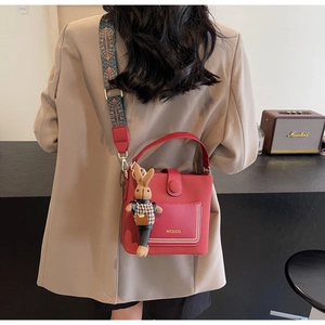 Detail of red bucket bag with wide ethnic style embroidery strap and rabbit charm