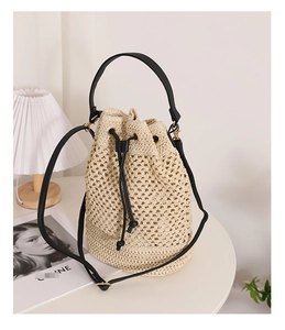 Detail of hand-woven straw bucket bag with black leather drawstrings and handles
