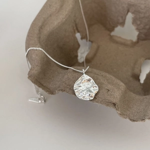 Close-up of 925 sterling silver organic textured round pendant on eco-paper background