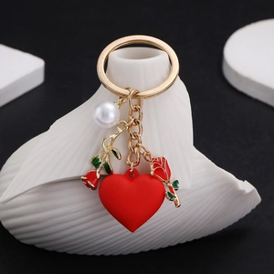 Golden keychain with red heart, rose pendant, and pearl hanging on white shell decor