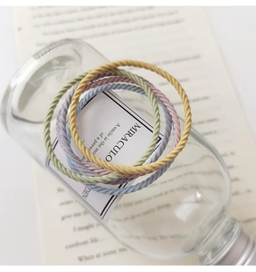 Close-up of four pastel elastic braided hair ties displayed on a clear glass bottle