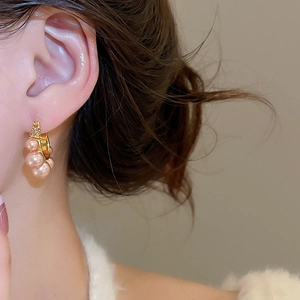 Gros plan de boucles d'oreilles dorées avec perles roses portées par un mannequin sur beige