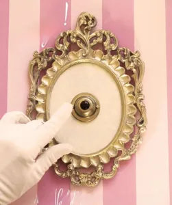 Detail of gloved hand pressing a vintage gold relief Press For Champagne button