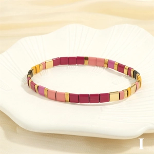 Macro view of colorful enamel Tila beads on elastic bracelet over shell plate