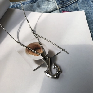 Macro detail of a silver fish hook pendant with a sparkling diamond on blue denim