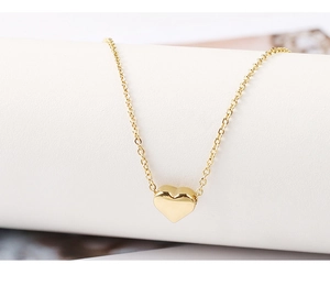 Close-up of a polished golden heart pendant necklace on a minimalist white stand