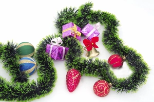 Close-up of dark green tinsel garland with assorted festive ornaments on white background