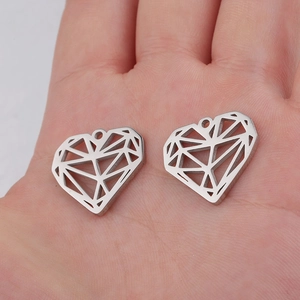 Detail showing two geometric hollow heart pendants held in palm for scale comparison