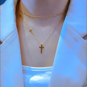 Detail view of double-layered gold cross necklace worn with a white blazer
