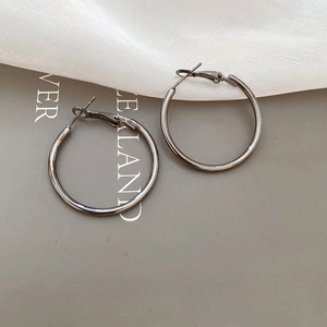 Detailed view of metallic gunmetal hoop earrings displayed on stylish beige fabric