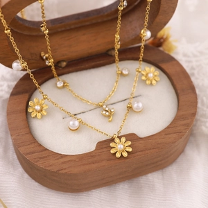 Collier plaqué or 18K avec marguerites et perles blanches sur un coffret à bijoux en bois