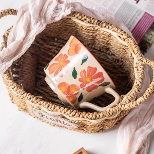 Ceramic floral coffee mug with hand-painted orange flowers in a rustic woven basket