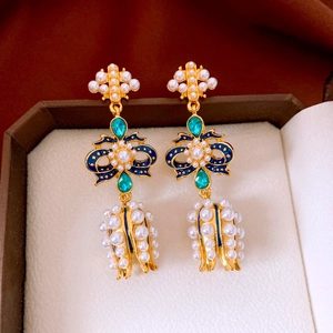 Detailed shot of vintage gold earrings with pearls and green gems in a jewelry box