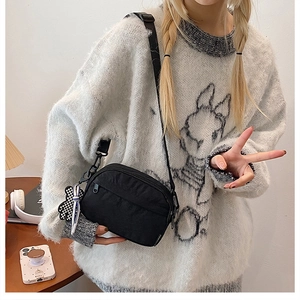 Détail du petit sac bandoulière noir en nylon avec pendentif ours sur mannequin femme