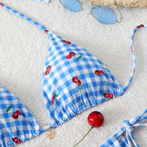 Detail of blue gingham bikini top with cherry print and golden flower pendant detail
