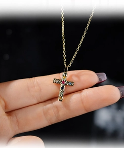 Detail view of gold cross pendant with colorful zircons held by hand for size