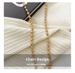 Detail shot of a shiny gold beaded metal chain for crossbody bags on white fabric