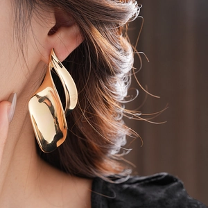 Close-up of model wearing large gold-tone streamlined leaf earrings with metallic finish
