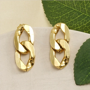 Close-up of chunky gold chain link earrings on a neutral tray with greenery
