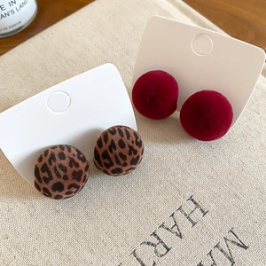 Detailed view of red and leopard print flocked round stud earrings on a beige fabric base