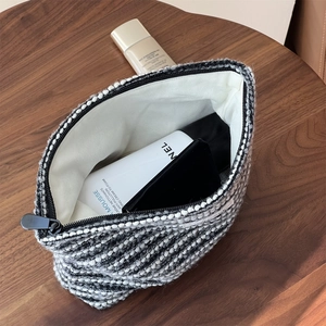 Large tweed makeup bag with black and white woven pattern and metal zipper on wood desk