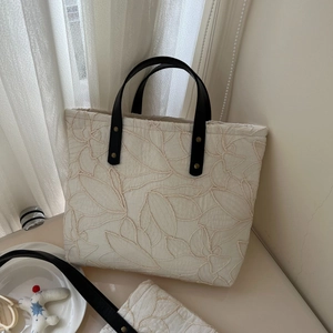 Detail of white canvas tote bag featuring leaf embroidery and black leather handle