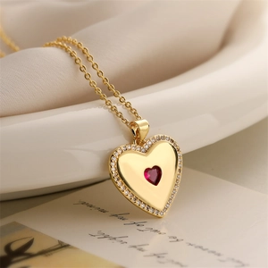 Close-up of gold plated heart necklace with red crystal and white pearls on elegant setup