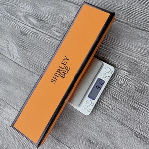 Weight measurement of a square watch gift box in orange and black showing 91.2g on a scale