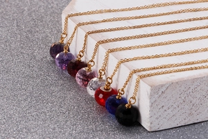 Detail of faceted colorful crystal ball pendants on gold chains arranged on a white stand