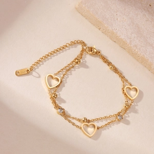 Detail of double-layer gold stainless steel bracelet with heart pendants and crystal accents
