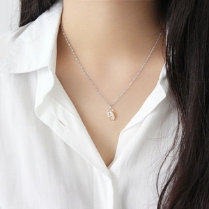 Detail of a natural Baroque pearl pendant on a thin silver chain worn over a white shirt