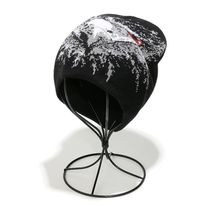 Detail of a black knit beanie showing white jacquard pine forest and snowy landscape pattern